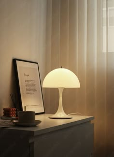 a table lamp sitting on top of a wooden dresser next to a framed photograph and coffee cup