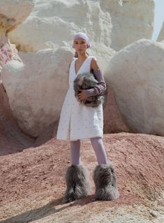 a woman standing on top of a rocky hill holding a stuffed animal in her hands