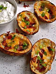 baked potato skins with bacon, cheese and green onions on a white surface next to a bowl of sour cream