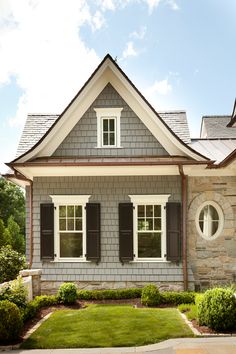 a gray brick house with white trim and shutters on the windows, grass in front