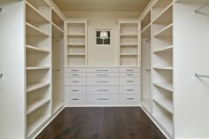 an empty walk in closet with white shelving and wood flooring on the side