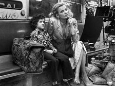 a woman sitting next to a child on a subway train while another person looks at the camera