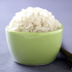 a green bowl filled with white rice next to chopsticks on a gray surface