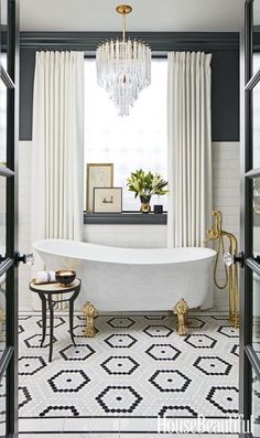 a white bath tub sitting under a chandelier in a bathroom next to a window