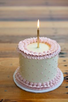 a birthday cake with a single candle on it's top, sitting on a wooden table