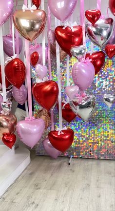 many heart shaped balloons are hanging from the ceiling in front of a colorful wall with sequins