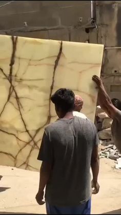 two men standing next to each other in front of a large slab of wood with cracks on it