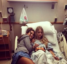 two people laying in a hospital bed with an iv machine on the wall behind them