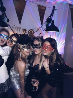 four women in masks posing for a photo at a masquerade party with lights on the wall behind them