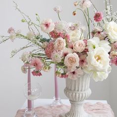 a white vase filled with lots of pink and white flowers on top of a table