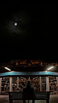 two people sitting on a bench at night with the moon in the sky above them