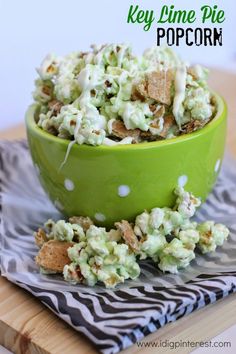 a green bowl filled with popcorn sitting on top of a wooden table next to a black and white napkin