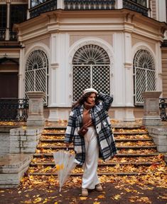 a woman is walking down the street with an umbrella in her hand and she's wearing a plaid coat