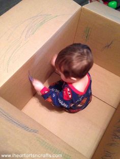 a small child in a cardboard box playing with colored crayons on the floor