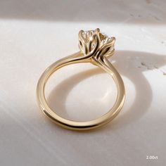 a yellow gold ring with a single diamond on the top, sitting on a white surface