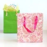 two shopping bags with pink and green handles on white table next to each other,