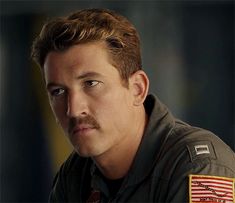 a man with a mustache and an american flag patch on his shirt is staring at the camera