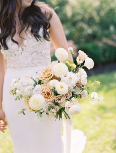 a woman holding a bouquet of flowers in her hand while standing on the grass outside