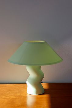 a green table lamp sitting on top of a wooden table next to a white wall