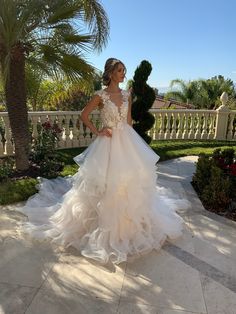 a woman in a wedding dress standing on a patio with palm trees and bushes behind her