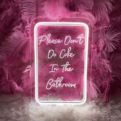 a neon sign that says please don't do cake in the bathroom on pink feathers