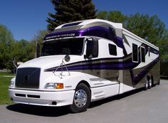 a white and purple rv parked on the side of a road next to some trees