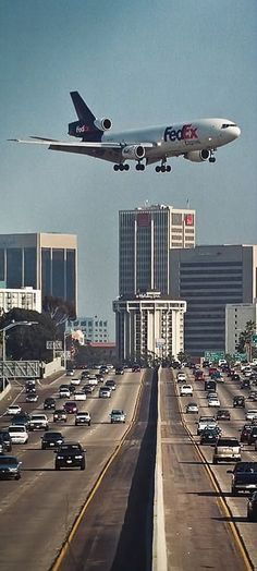 an airplane is flying over a busy freeway in the middle of the day with buildings and cars on both sides