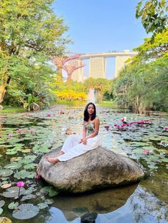 a woman sitting on top of a rock in the middle of a pond filled with water lillies