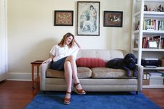 a woman sitting on top of a couch next to a black dog in a living room