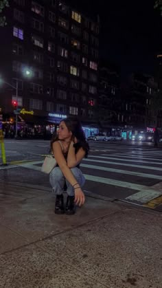 a woman sitting on the ground in front of a crosswalk at night with her head down