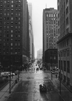 a black and white photo of a city street with tall buildings on either side of the road