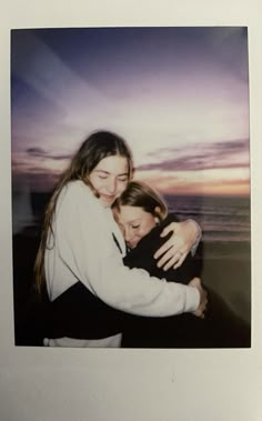 two young women hugging each other on the beach at sunset, with an ocean in the background