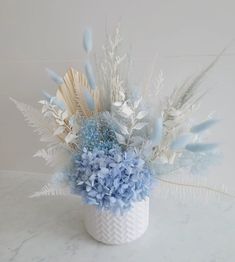 a white vase filled with blue flowers and feathers