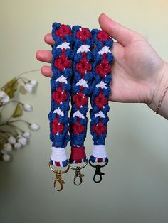 a hand holding two pairs of red, white and blue crocheted key fobs