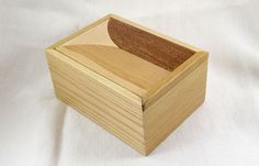 a wooden box with a curved lid on a white cloth covered tablecloth, it is made out of wood and has been cut in half to show the shape