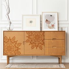 a wooden cabinet with two pictures on top of it next to a rug and vase