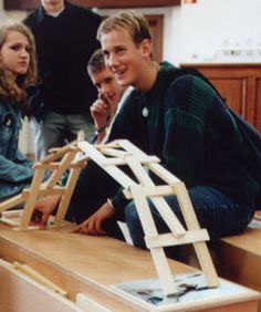 a group of young people standing around a wooden structure on top of a countertop