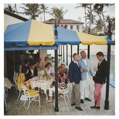 two men standing under a blue and yellow tent next to other people eating at tables