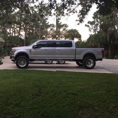 a silver truck parked on the side of a road in front of trees and grass