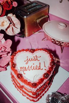 a heart shaped cake sitting on top of a table next to pink flowers and a toaster