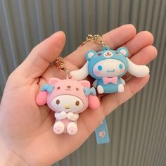 someone holding two hello kitty keychains in their hand, one is blue and the other is pink