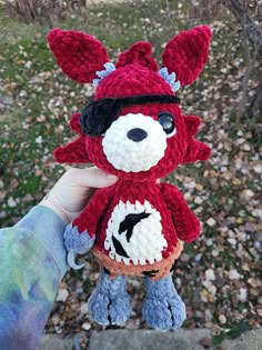 a hand holding a crocheted stuffed animal in the shape of a fox with horns