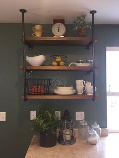 a kitchen with green walls and shelves filled with plates, bowls, cups and utensils