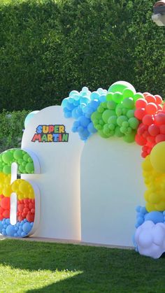 an arch made out of balloons with the letters super mario on it is in front of some bushes