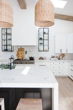 a white kitchen with two hanging lights over the stove and counter top, along with wooden stools