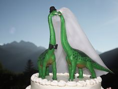 two green dinosaur figurines kissing on top of a wedding cake with mountains in the background