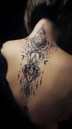 the back of a woman's neck with an intricate tattoo design on her lower back