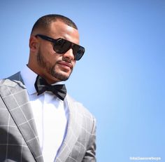 a man in a suit and sunglasses looks off into the distance while standing against a blue sky