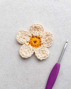 a crocheted flower with an orange center sits next to a purple knitting needle