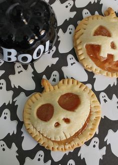 two halloween pies with faces on them sitting on a table next to a black bowl